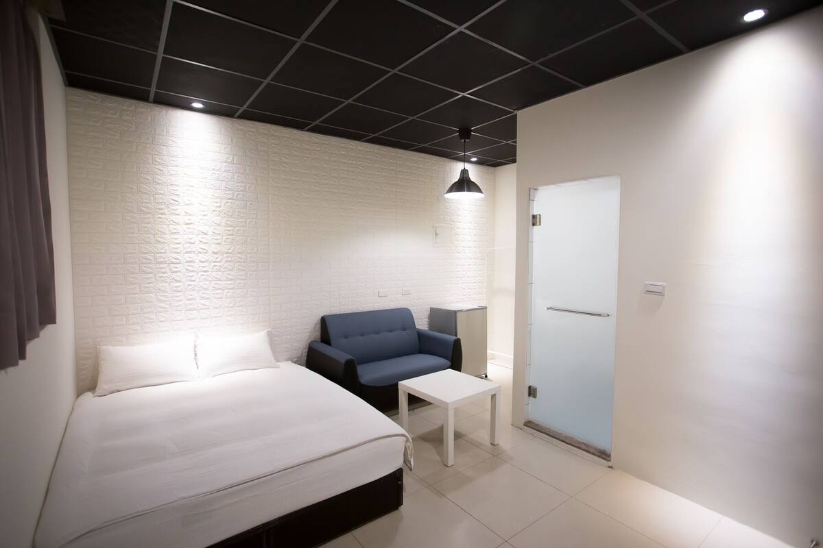 A bedroom with a bed, a blue chair, a small table, and a white door.