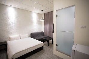 Een hotelkamer met een bed, een slaapbank, een klein tafeltje, een televisie en een deur.
