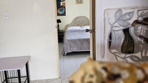 Una habitación con una cama, una mesa y una silla. Hay una puerta que da a otra habitación.