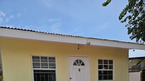 Un edificio de una planta con una puerta blanca, dos ventanas y un pequeño porche.