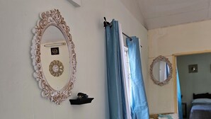 Una habitación con una cama, un espejo, una estantería con un reloj y una ventana con cortinas.