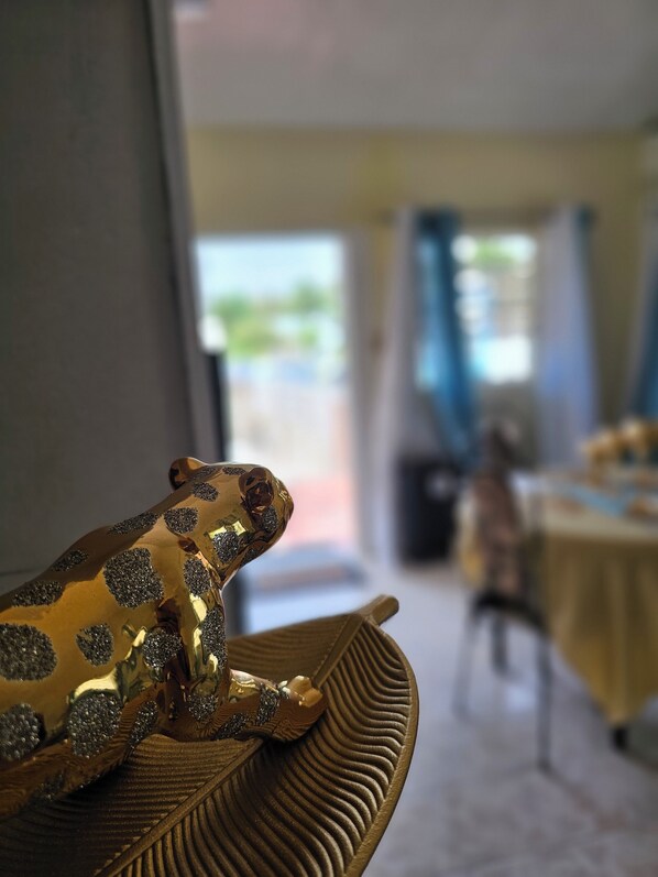 Eine goldene Froschstatue auf einer strukturierten Oberfläche vor verschwommenem Hintergrund mit einem Tisch und einem Stuhl.