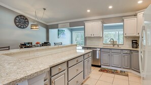 A kitchen with a large island, white cabinets, a clock, and a window. - Saltwater Pool! Sebring Oasis Near Lake Jackson (Sebring)