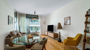 Un salon moderne avec une table à manger en verre, un canapé et un téléviseur posé sur un meuble en bois.