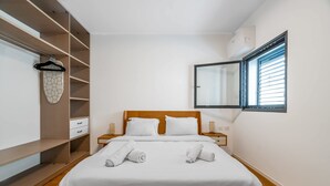 Un lit bien fait, avec deux serviettes, une tête de lit en bois, une table de chevet et un fer à repasser suspendu.
