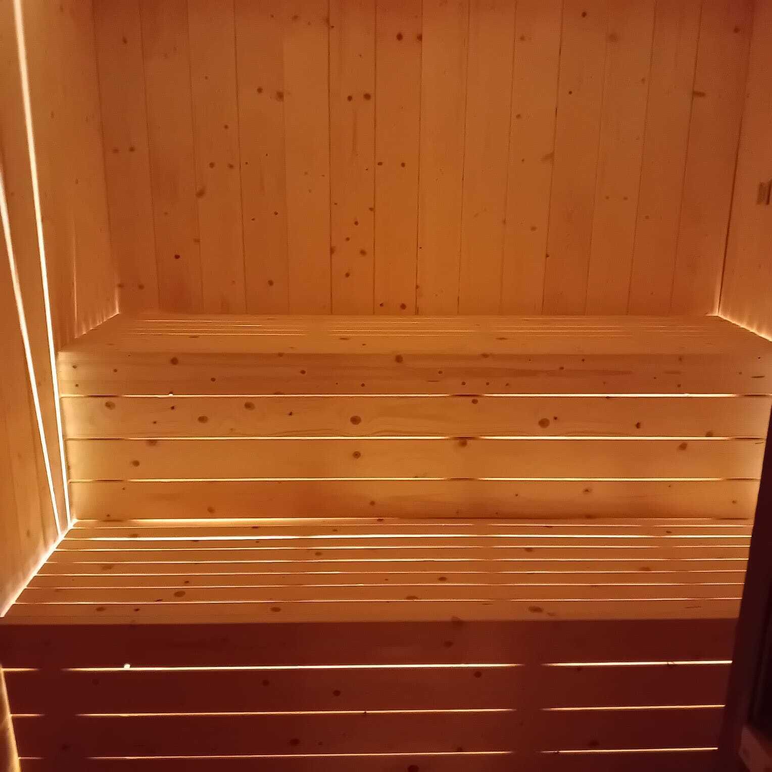 A wooden sauna with a sloped floor and a warm, inviting glow.