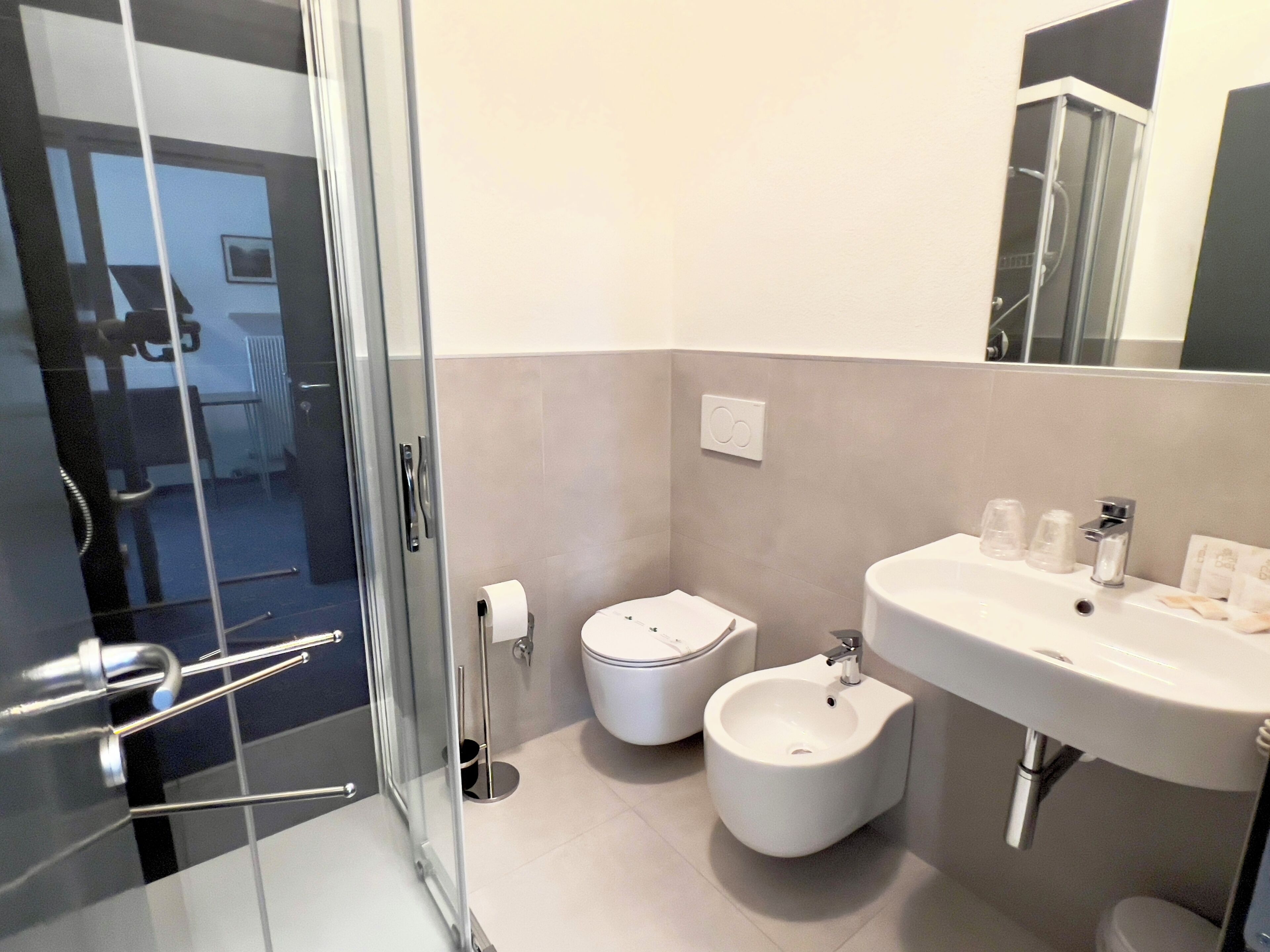 A modern bathroom with a glass shower enclosure, a toilet, bidet, and a sink with a mirror above.