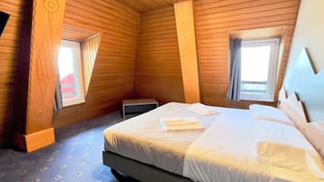 A wooden room with a bed, two windows, and a small table.