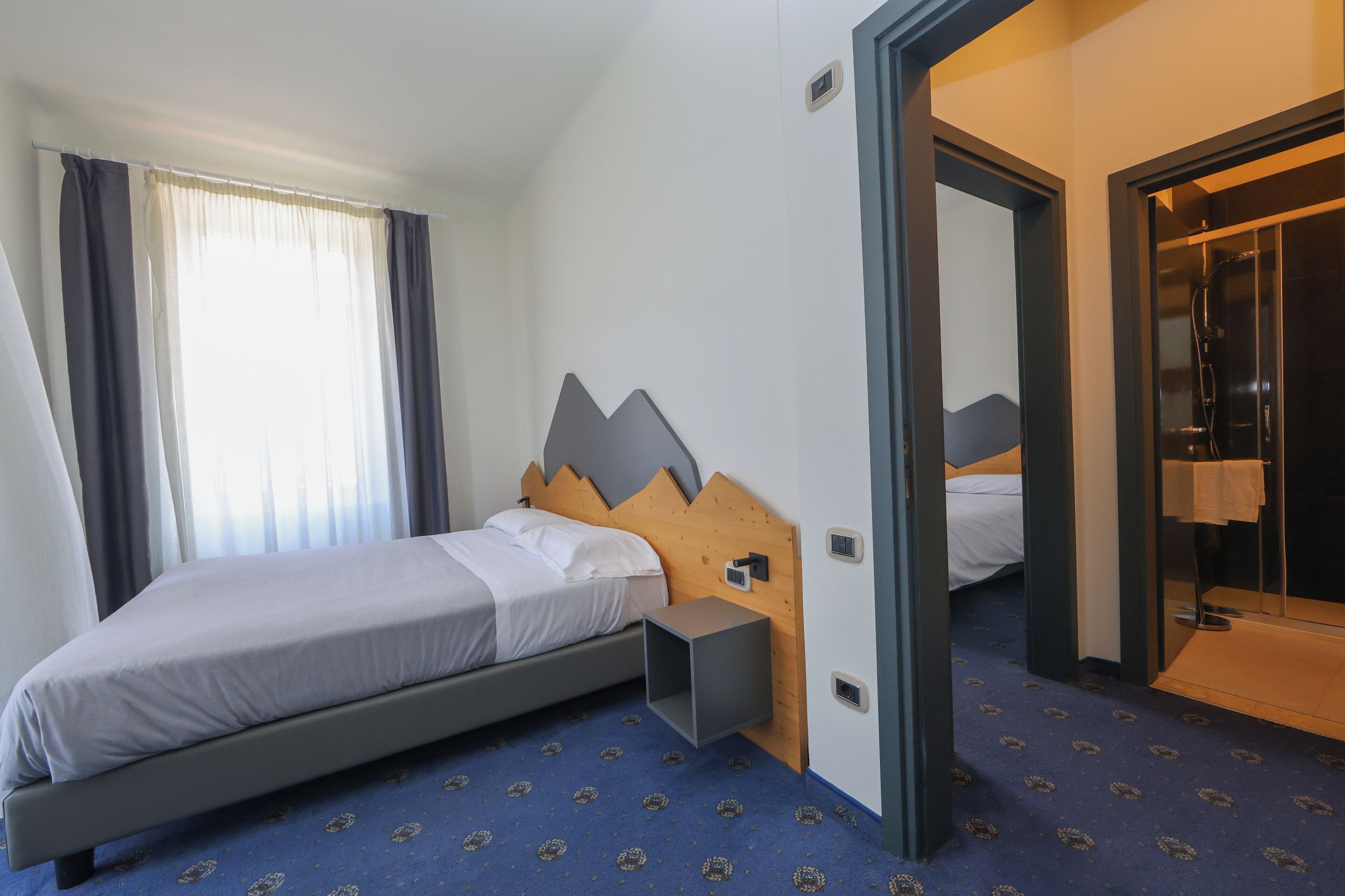 Habitación de hotel con cama, mesita de noche, ducha y baño con puerta de vidrio.