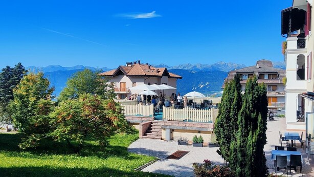A hotel with outdoor seating, a view of mountains, and a garden area. - HOTEL REGINA DEL BOSCO (Ronzone)