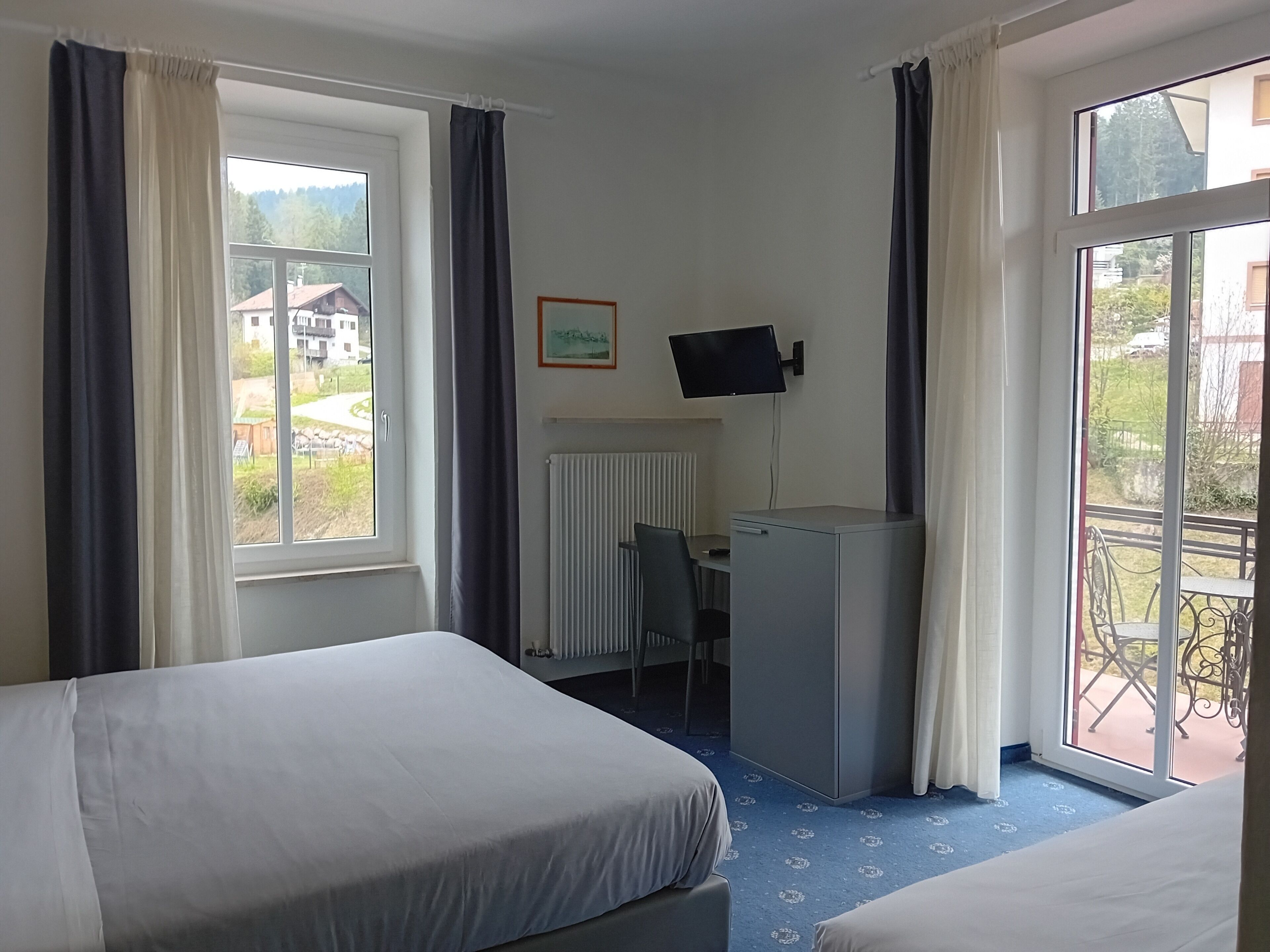 A hotel room with two beds, a desk with a computer, a TV, and a balcony with outdoor furniture.