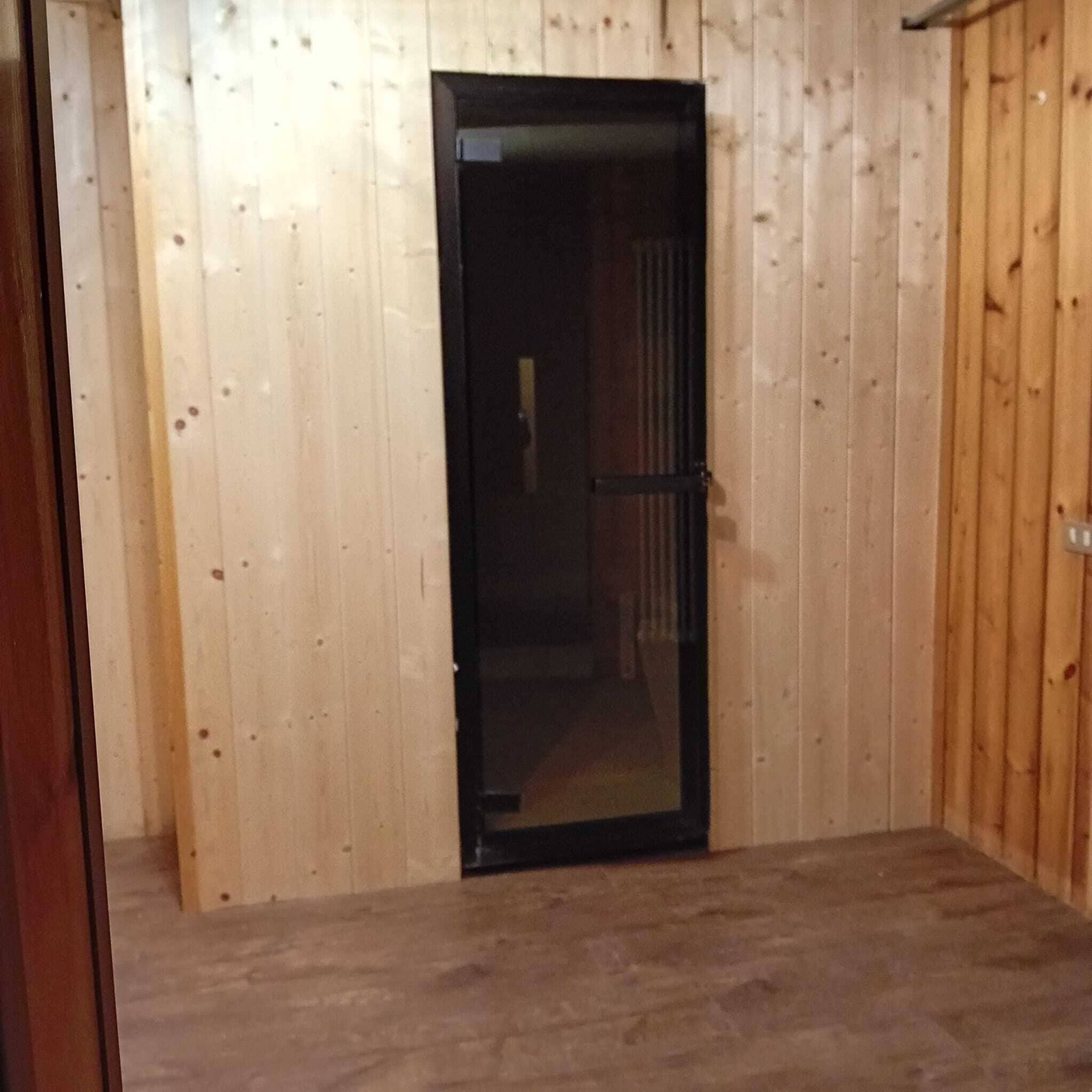 A wooden-paneled room with a black door and a visible interior.