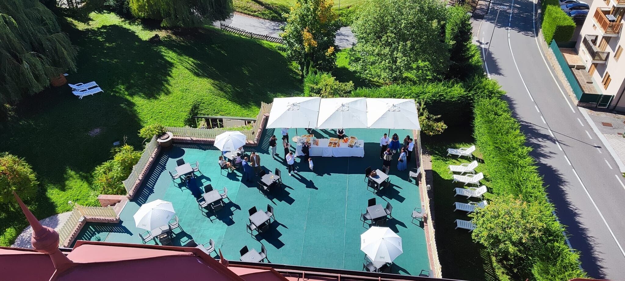 Un área de piscina al aire libre con sillas de descanso y sombrillas, rodeada de vegetación y una carretera.
