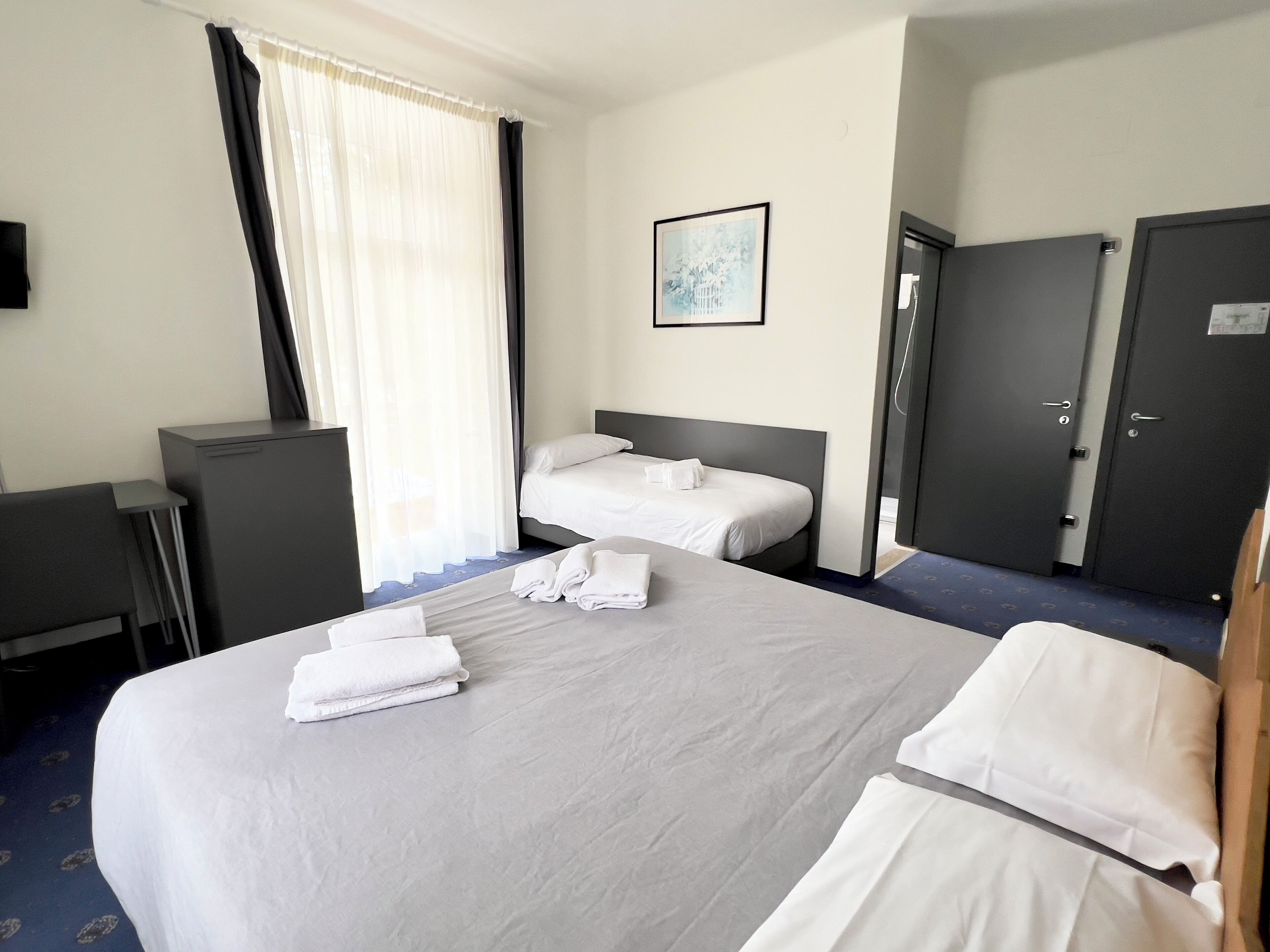 Camera d'albergo con due letti, una scrivania, un armadio e una finestra con tende.