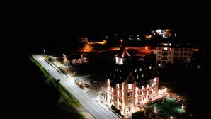 A multi-story hotel with a central courtyard, a swimming pool, and a well-lit street. - HOTEL REGINA DEL BOSCO (Ronzone)