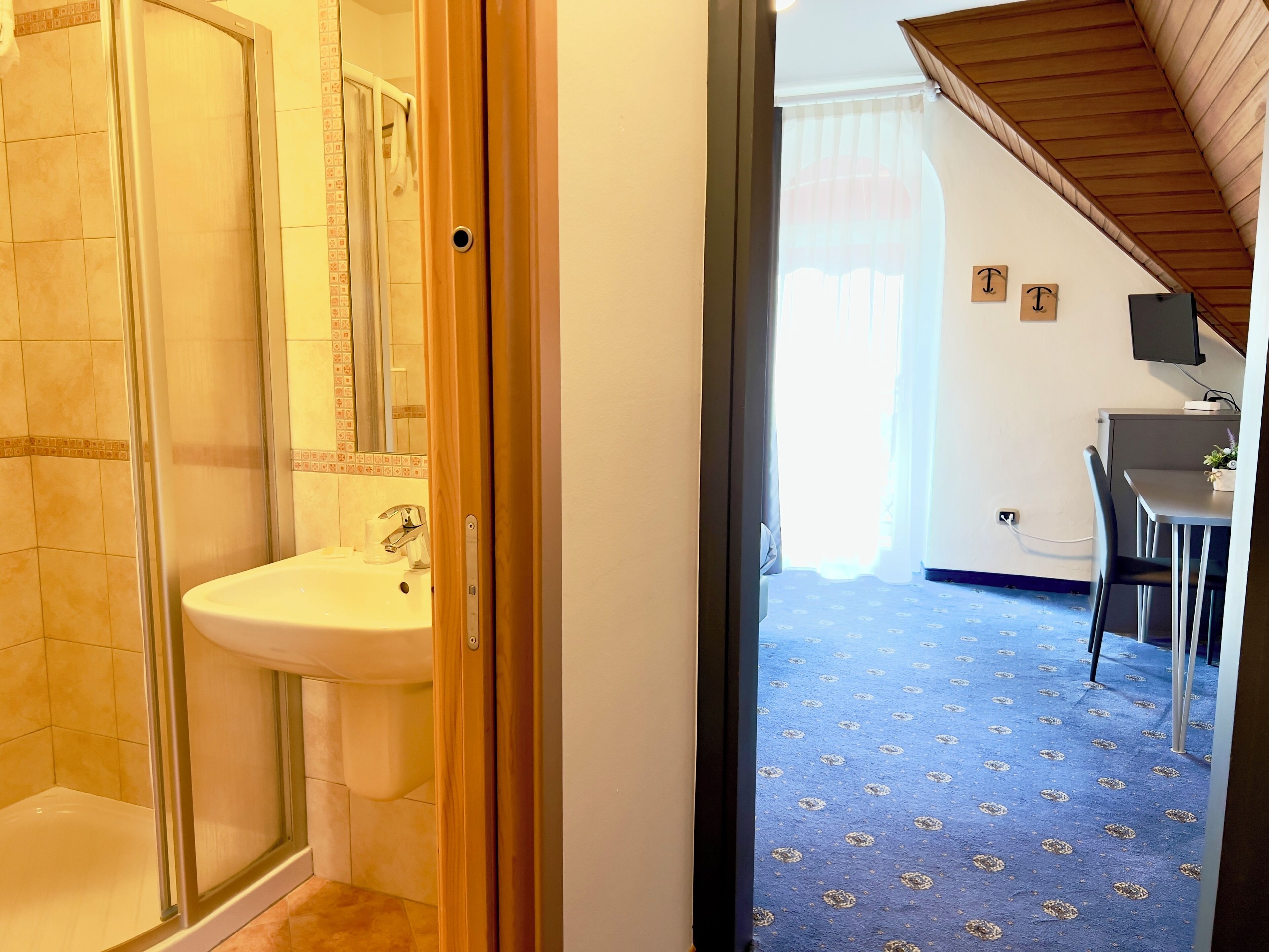 Un baño con cabina de ducha de vidrio, un lavabo y un inodoro. Hay una puerta de madera que da a una zona de comedor con mesa y sillas.