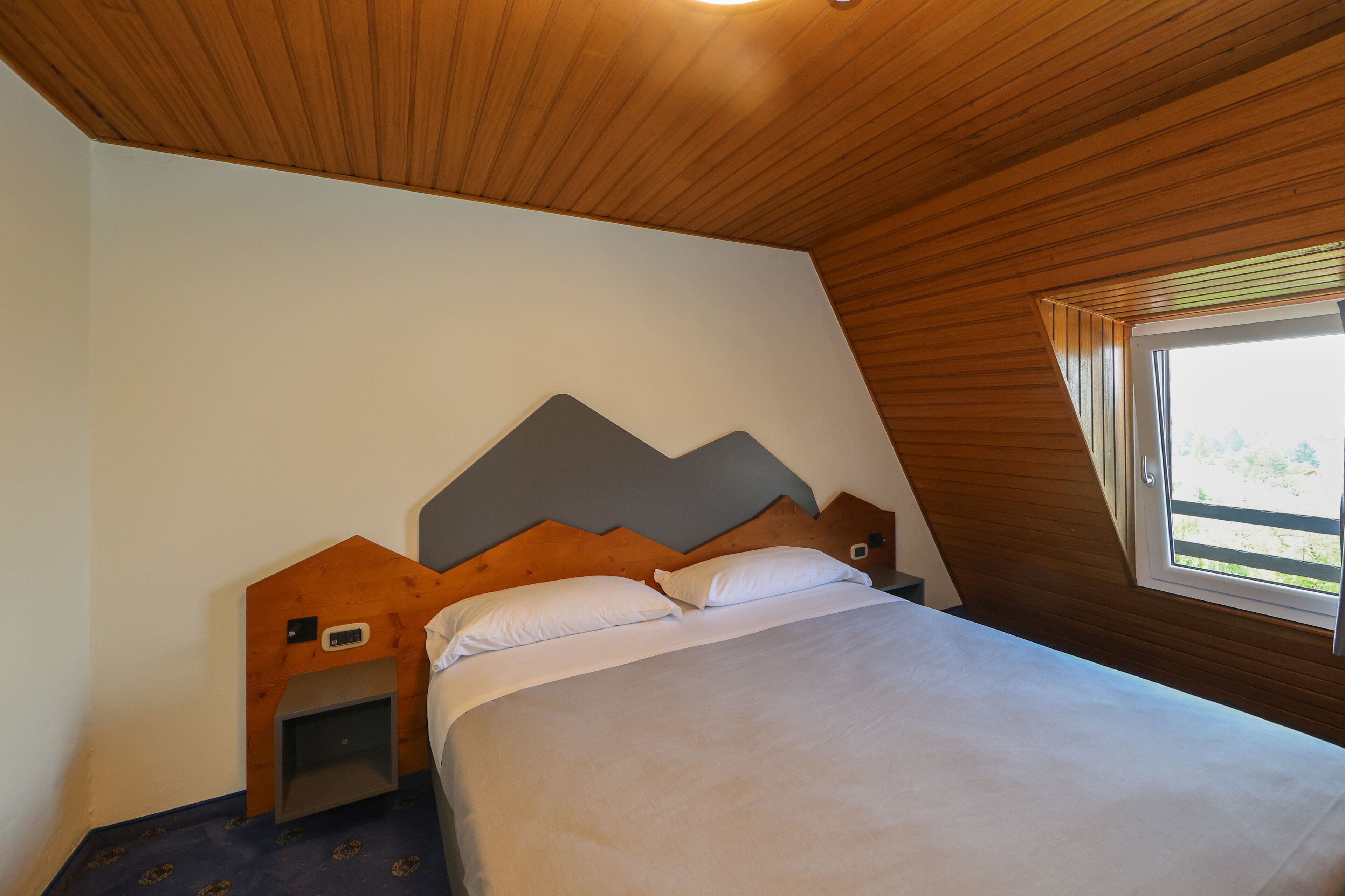 Une chambre avec un plafond en pente, un lit avec une literie blanche, une tête de lit en bois et une petite table de chevet.