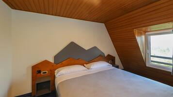 Une chambre avec un plafond en pente, un lit avec une literie blanche, une tête de lit en bois et une petite table de chevet.