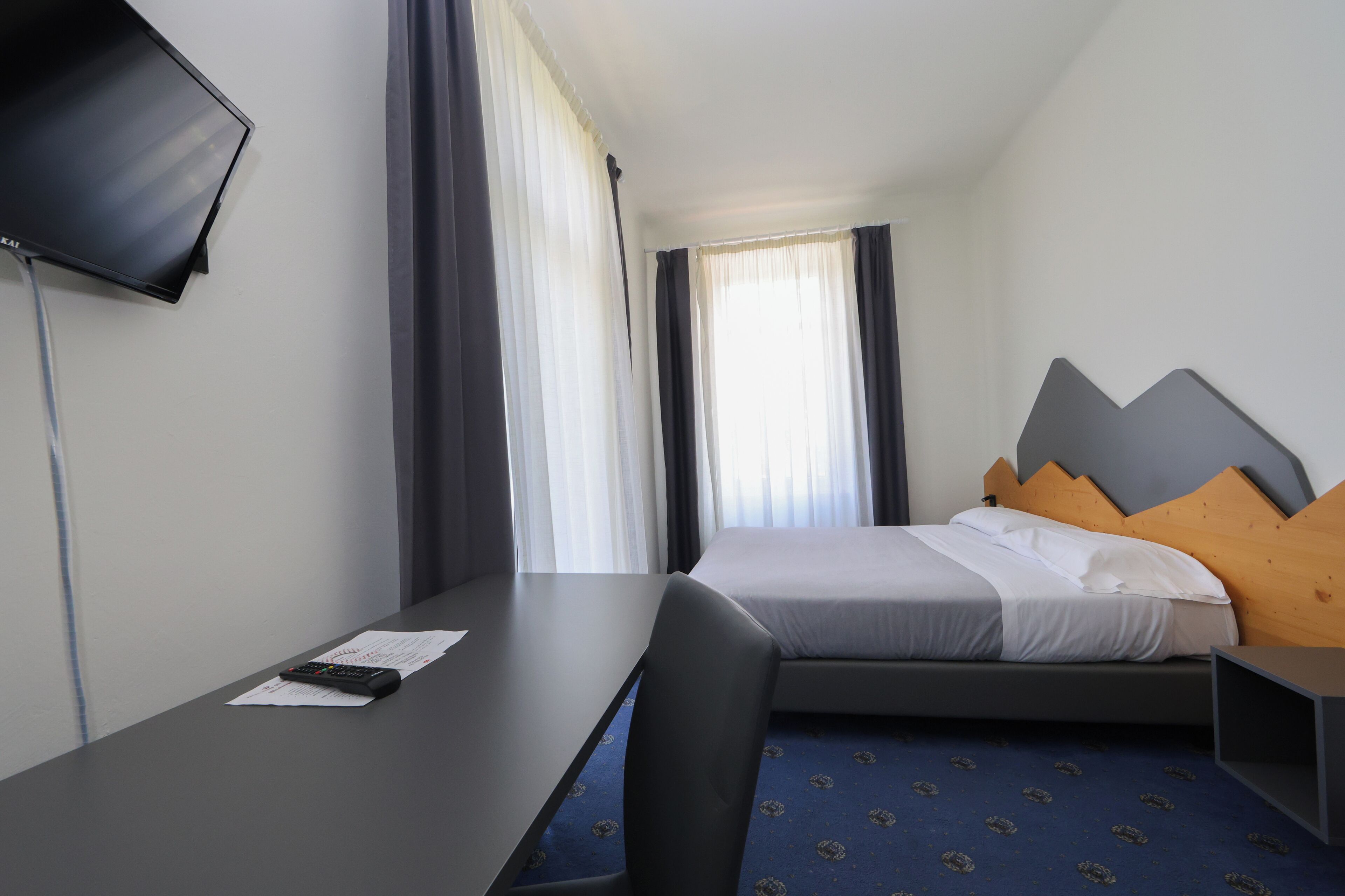 Hotellihuone, jossa on sänky, työpöytä, tuoli, televisio ja ikkuna, jossa on verhot.