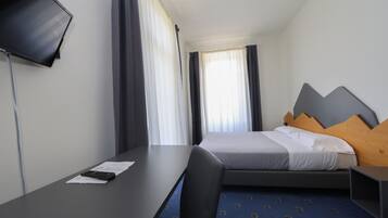 Hotellihuone, jossa on sänky, työpöytä, tuoli, televisio ja ikkuna, jossa on verhot.
