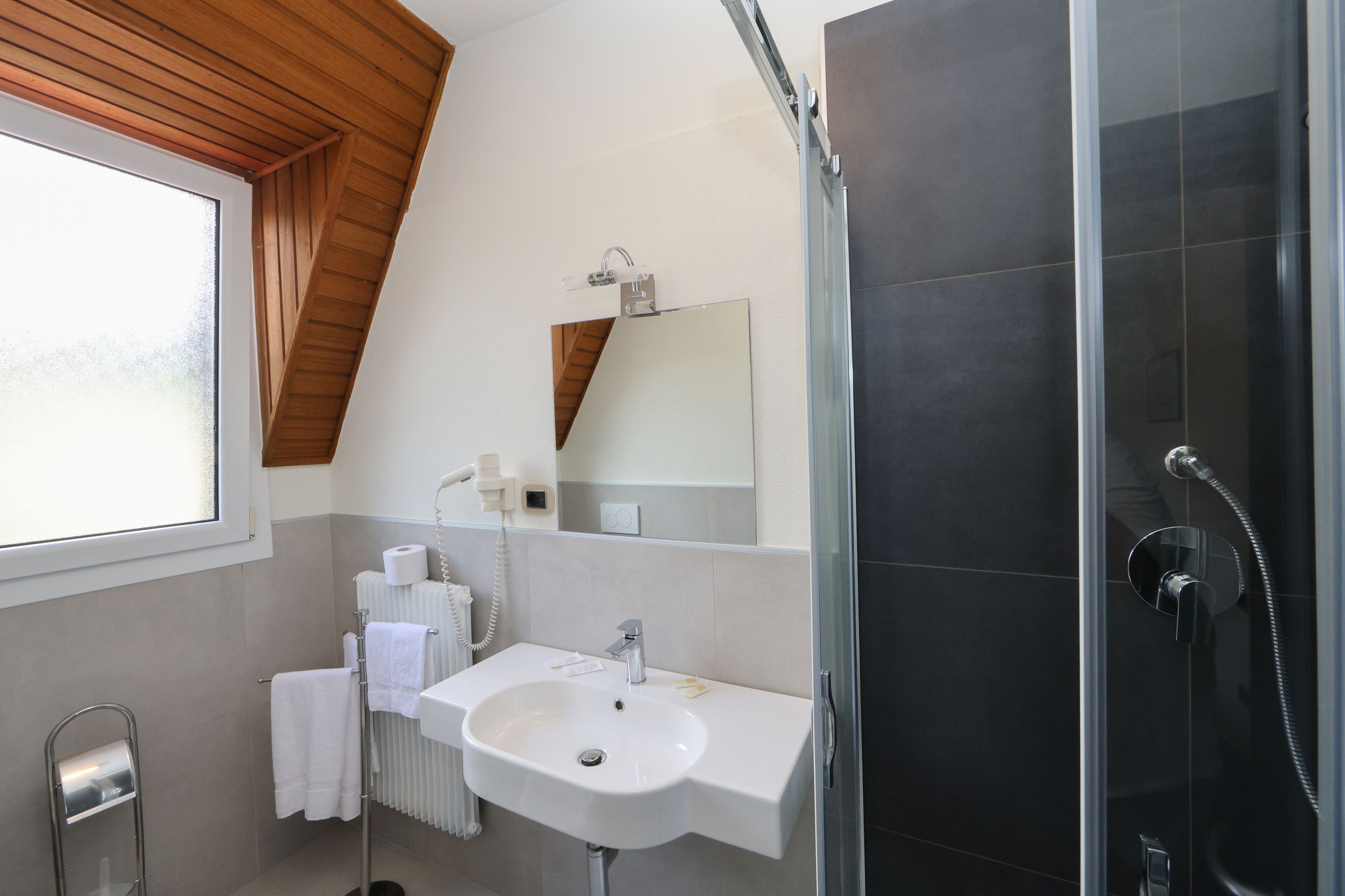 Un baño moderno con un lavamanos blanco, un espejo, un perchero para toallas y una zona de ducha.