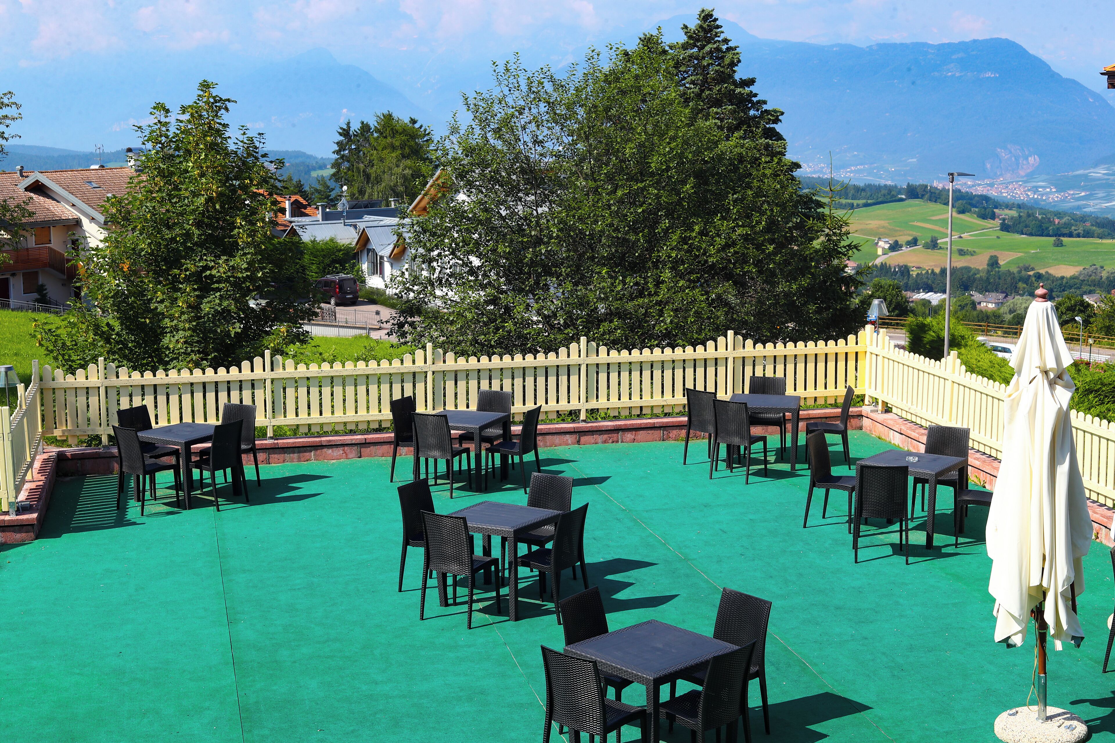 Eine Außenpatio mit Tischen und Stühlen, ein weißer Zaun und ein Blick auf eine Stadt und Berge im Hintergrund.