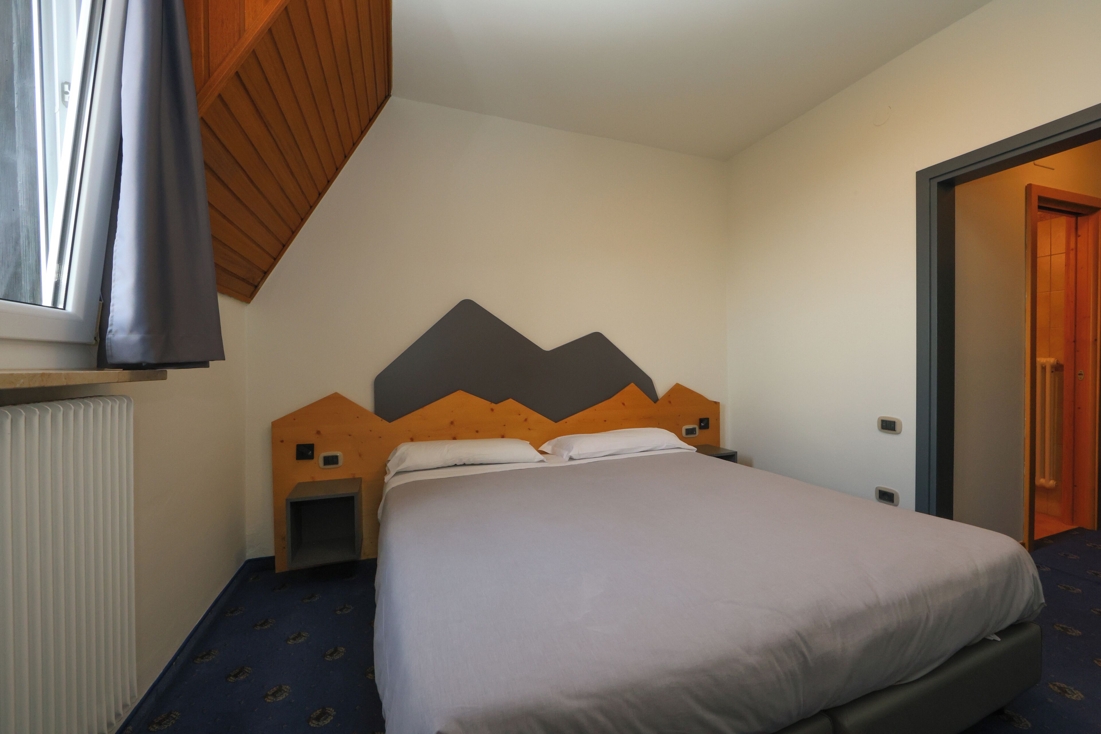 A bedroom with a bed, a wooden headboard, a radiator, and a door leading to another room.