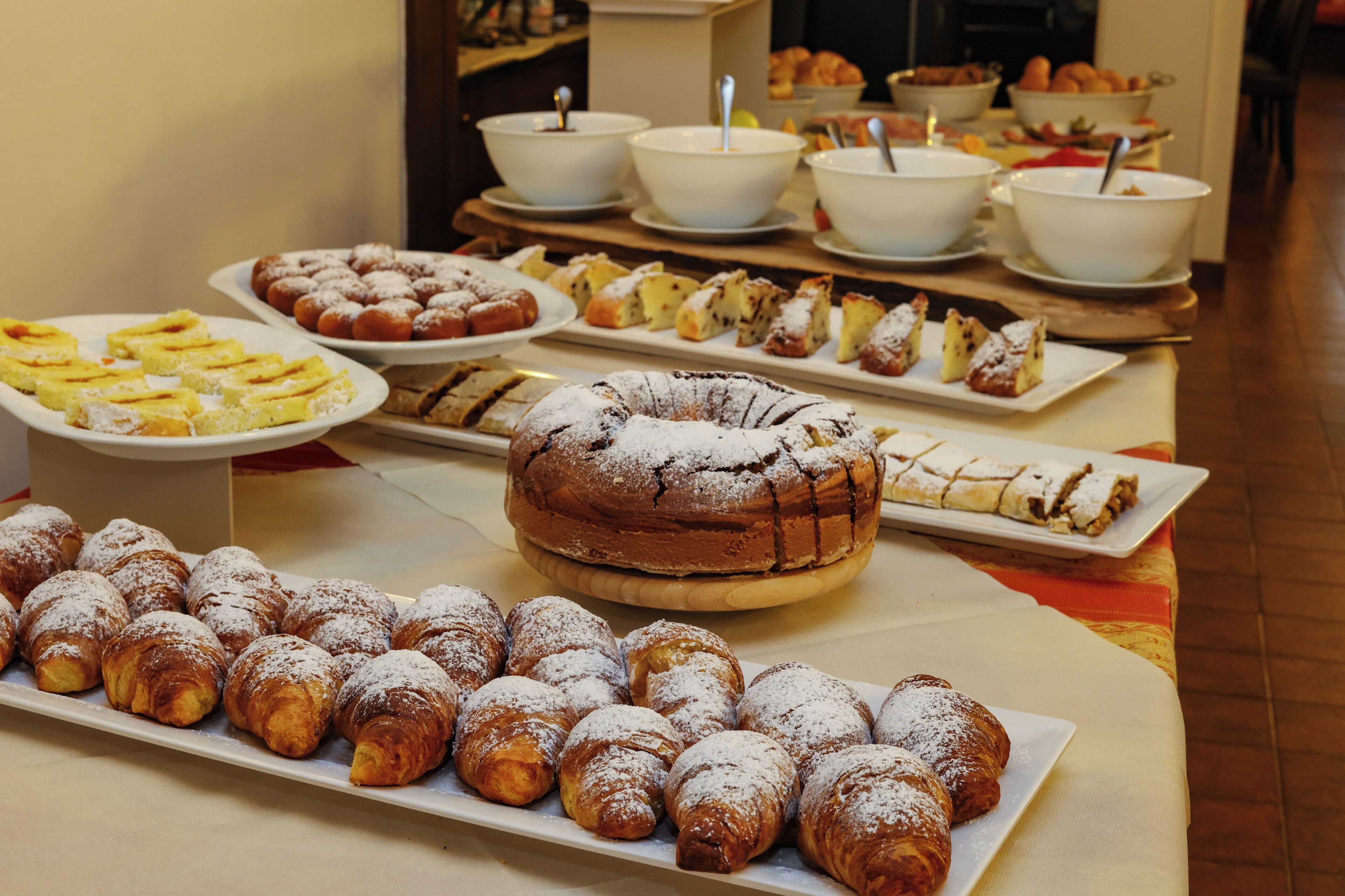 A buffet table with various pastries and desserts, including croissants, a bundt cake, and other baked goods.
