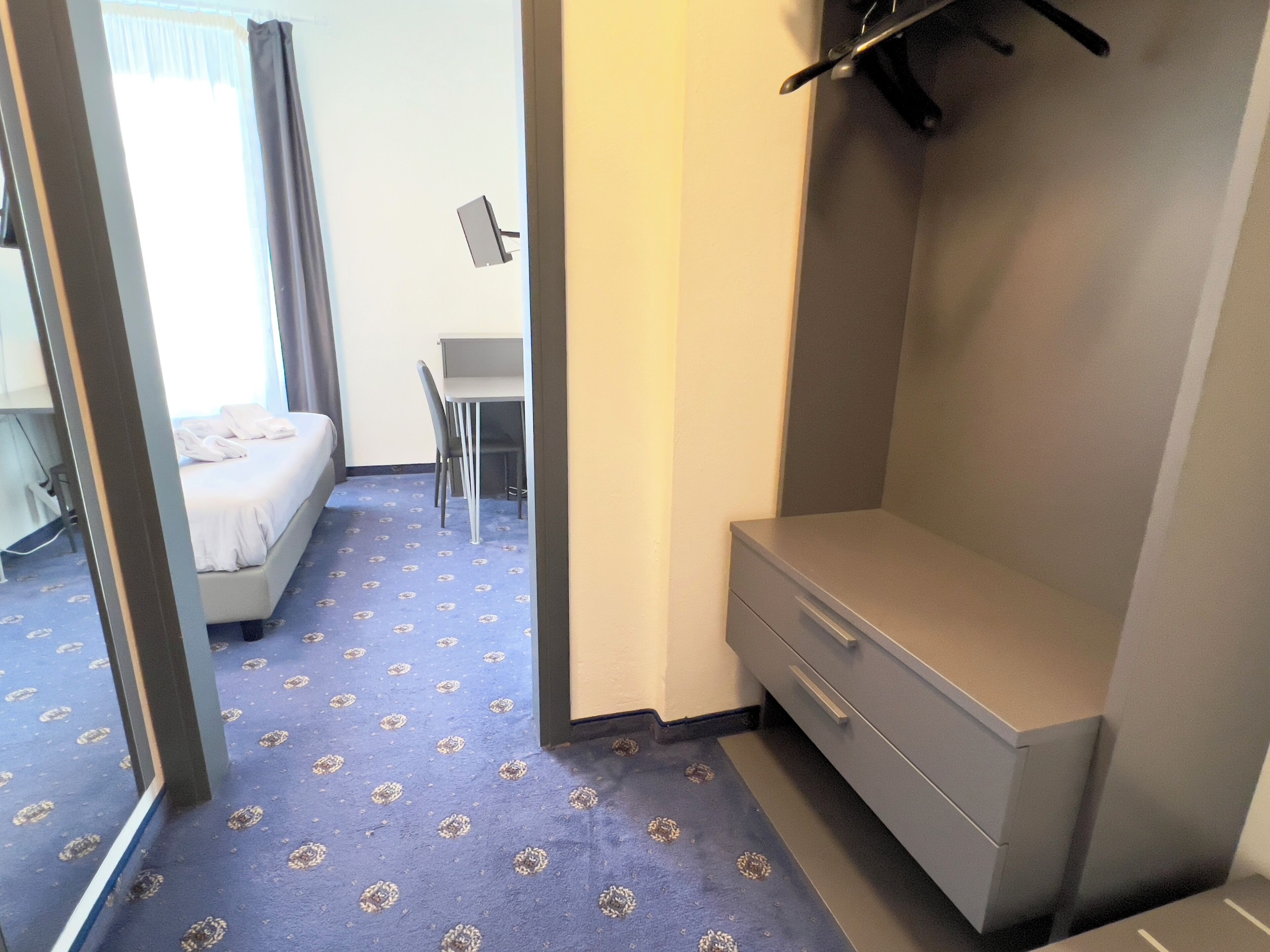 A hotel room with a bed, a desk, a chair, and a wardrobe.
