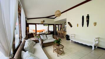 A spacious living area with a large sofa, wicker furniture, and a dining area visible through an open door.