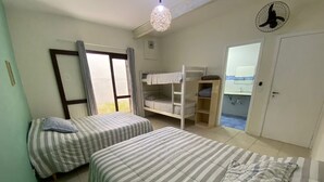 A bedroom with two beds, a bunk bed, a fan, a window with curtains, and a door leading to a bathroom. - Complete house in Maresias, 450m from the sand (SÃO SEBASTIÃO)