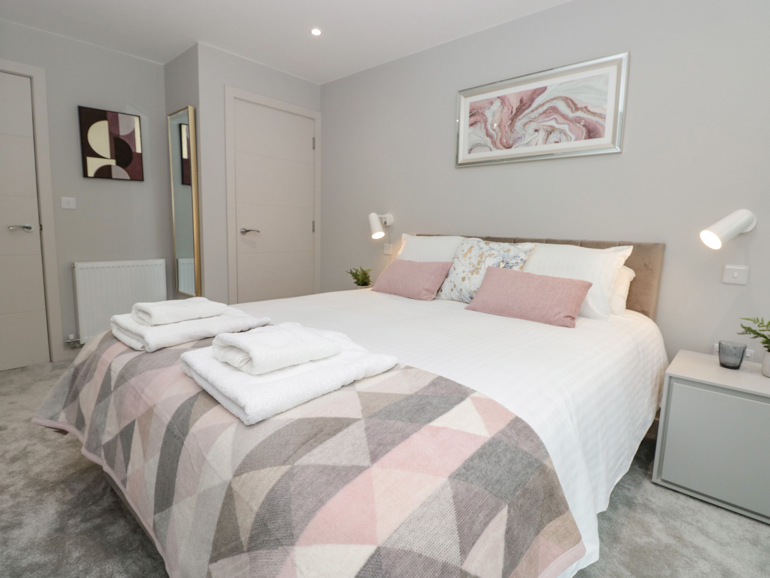 A neatly arranged bedroom with a bed, bedside tables, and a mirror.