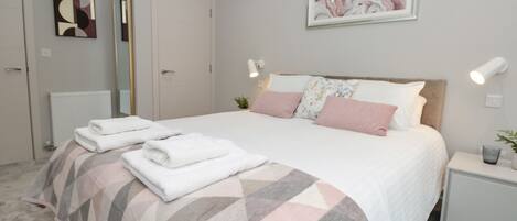 A neatly arranged bedroom with a bed, bedside tables, and a mirror.
