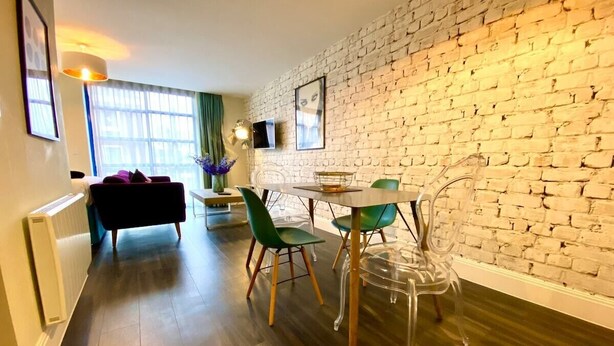 Ein modernes Wohnzimmer mit Backsteinwand, einer Essecke inklusive Tisch und Stühlen sowie einem Sofa.