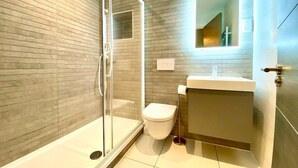 Ein modernes Badezimmer mit Duschkabine aus Glas, Toilette und Waschbecken mit Spiegel darüber.