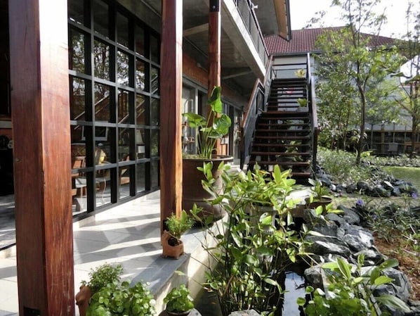 A modern building with large glass windows, a wooden staircase, and a landscaped garden with rocks and plants.