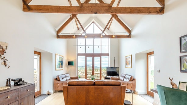 A spacious living room with a large sofa, a television, and a view of the outdoors through large windows.