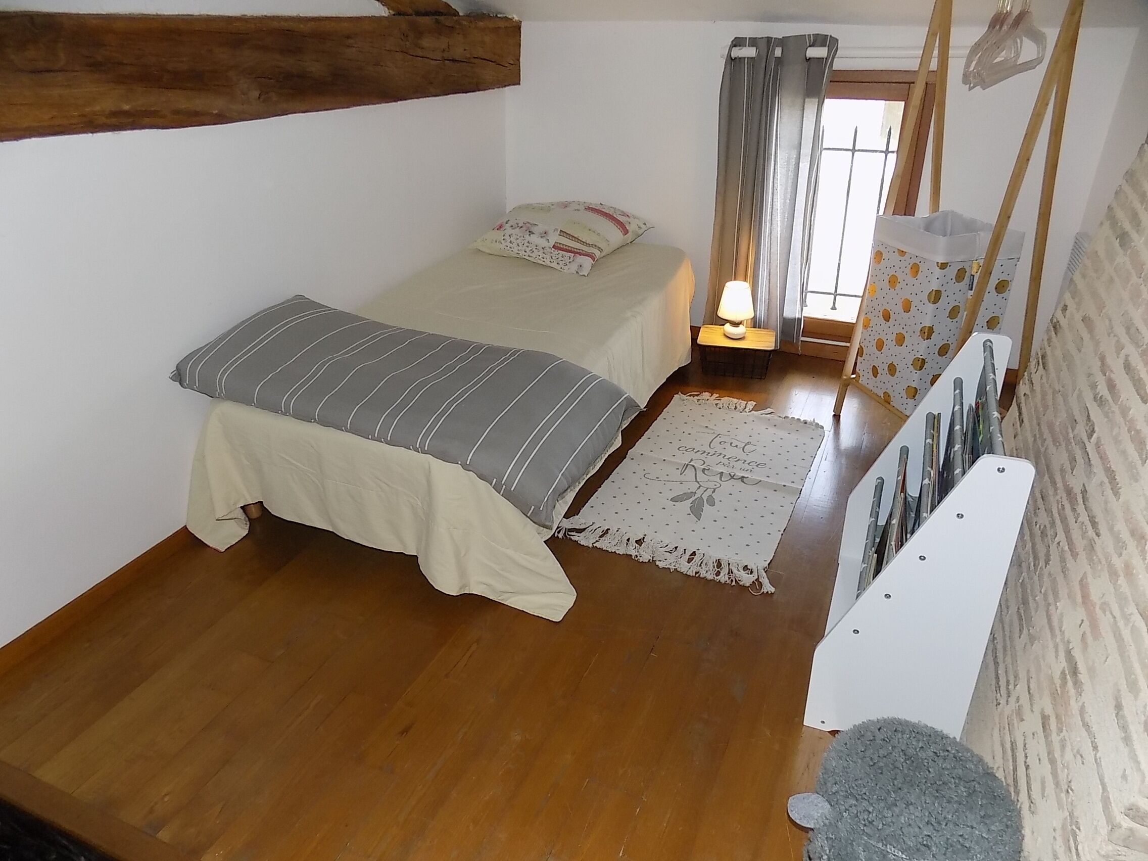 Un dormitorio pequeño y acogedor con una cama individual, una mesita de noche con lámpara y una ventana con cortinas.