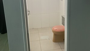 A bathroom with a toilet, a shower, and a small shelf. - Light Motel (Guarulhos)