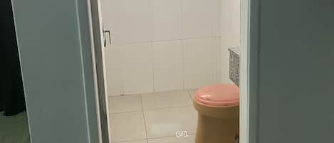 Un baño con inodoro, ducha y un estante pequeño.