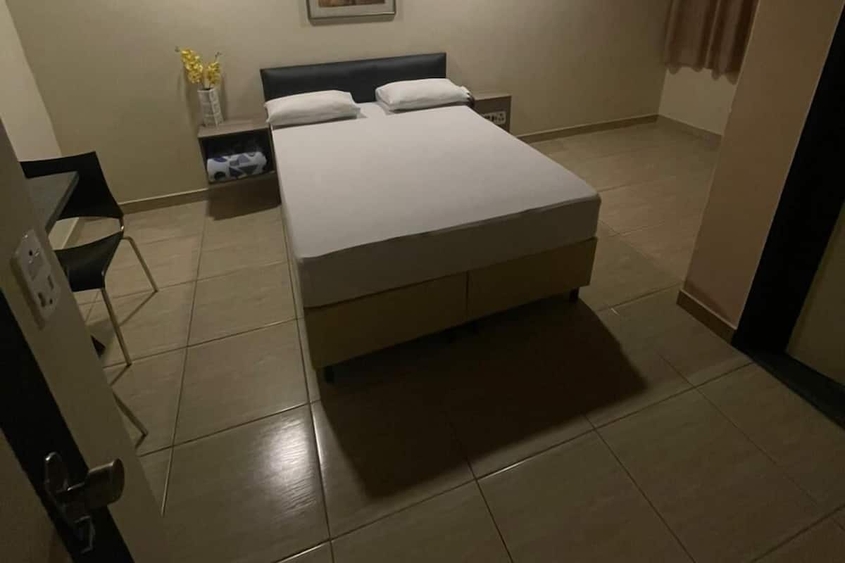 A bedroom with a bed, a nightstand, a wall-mounted picture, and a window with curtains.