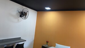 A hotel room with a bed, a desk, chairs, a nightstand, and a wall-mounted fan. - Light Motel (Guarulhos)