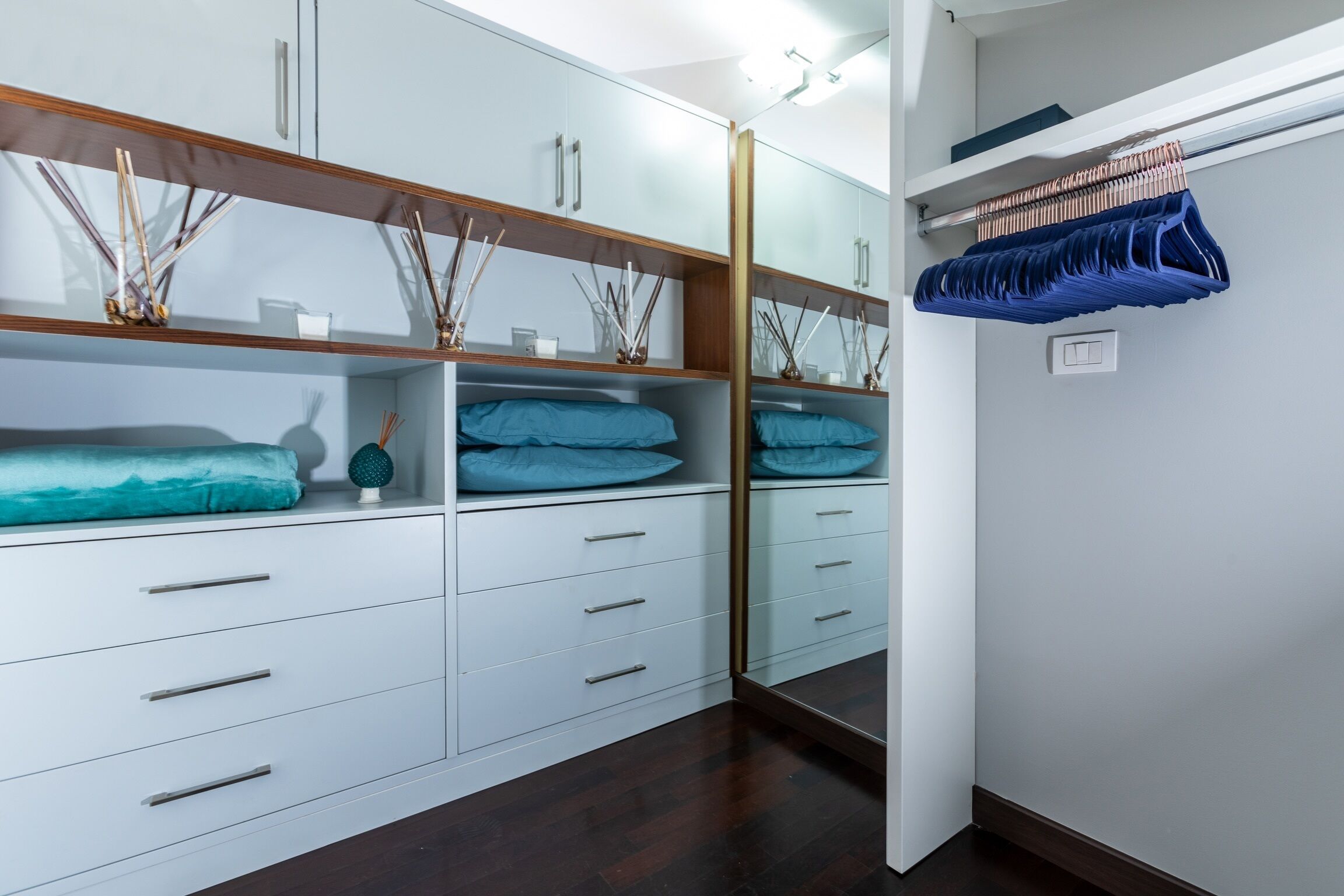 Un placard moderne avec des meubles blancs, un miroir et un organiseur suspendu bleu.