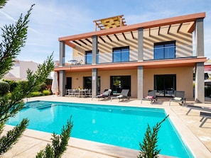 Une maison moderne à deux étages dotée d’une piscine, d’un espace salon extérieur et d’une pergola.