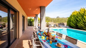 An outdoor dining area with a pool, featuring a table set with breakfast and a view of the pool and greenery. - Villa with heatable pool, 2 jacuzzis & BBQ (Armação de Pêra)