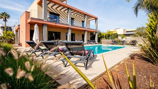 A modern building with a pool, lounge chairs, and a covered patio area. - Villa with heatable pool, 2 jacuzzis & BBQ (Armação de Pêra)