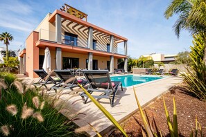Un bâtiment moderne doté d’une piscine, de chaises longues et d’un patio couvert.