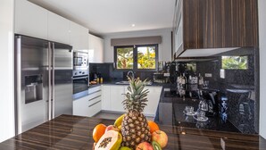 A modern kitchen with stainless steel appliances, a fruit bowl on the counter, and a view of the outdoors through large windows. - Villa with heatable pool, 2 jacuzzis & BBQ (Armação de Pêra)