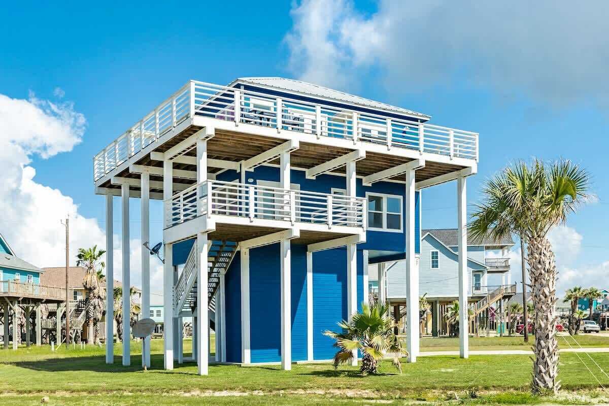 A blue building with a balcony, a staircase, and a palm tree in front.