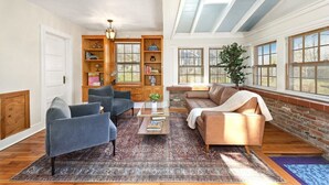 A spacious living room with a large window, a fireplace, and a bookshelf. - Cottage on Rush - Heart of Fayetteville (Fayetteville)